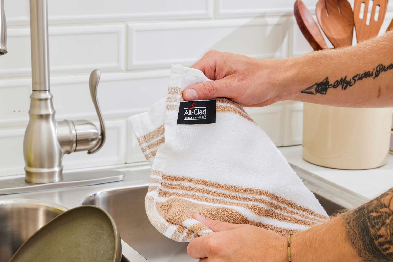 A person showing the tag of an All-Clad kitchen towel.