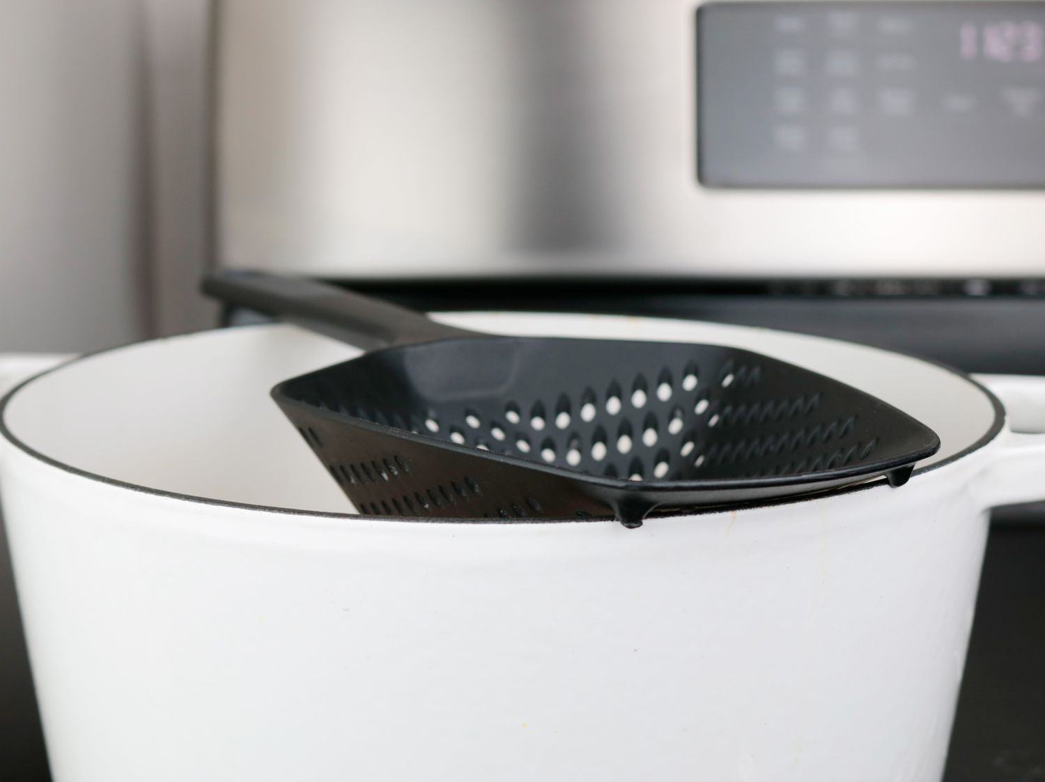 The colander spoon resting on the lip of a Dutch oven