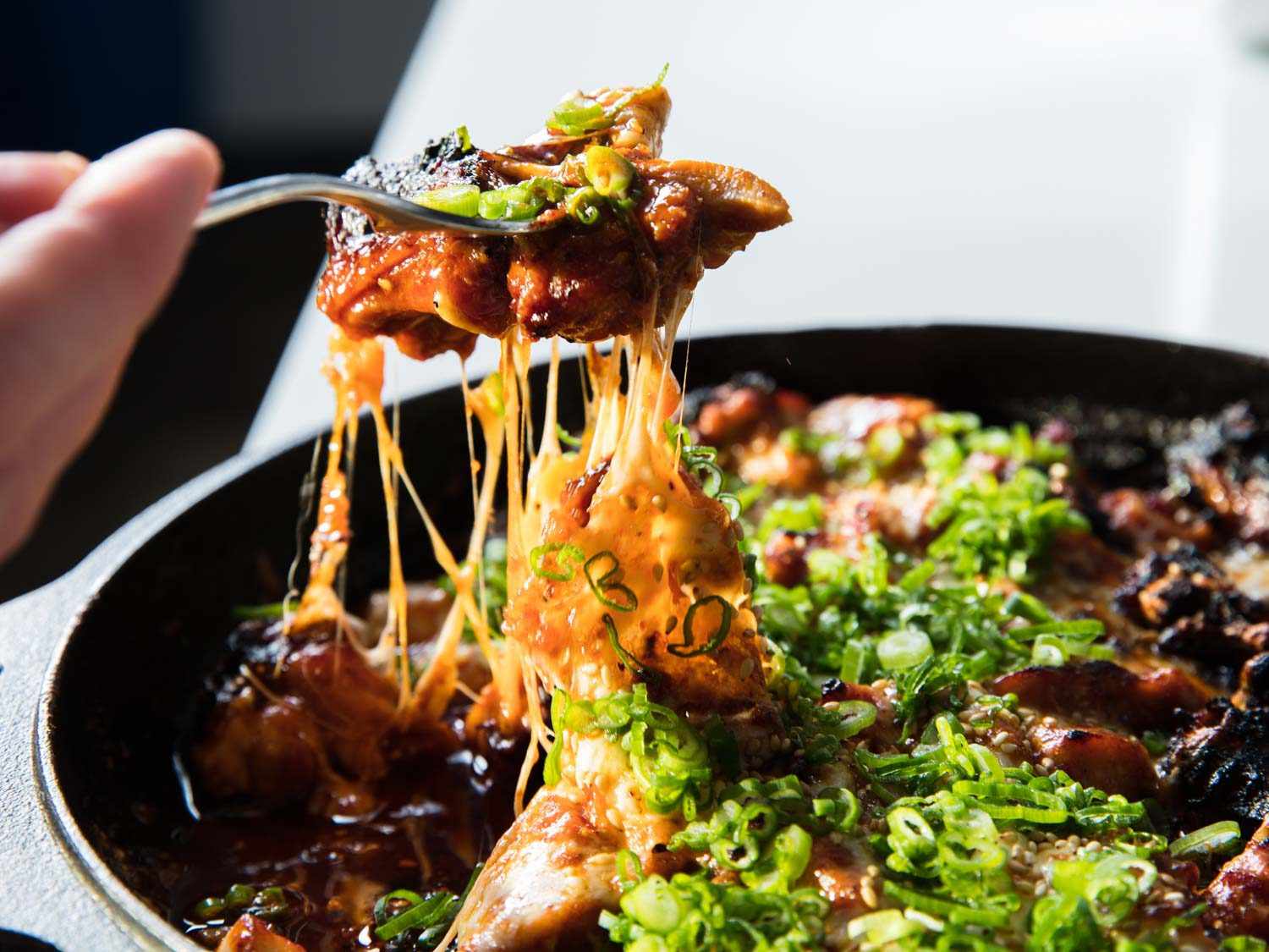 Fork full of chicken and melted cheese being lifted from a pan.
