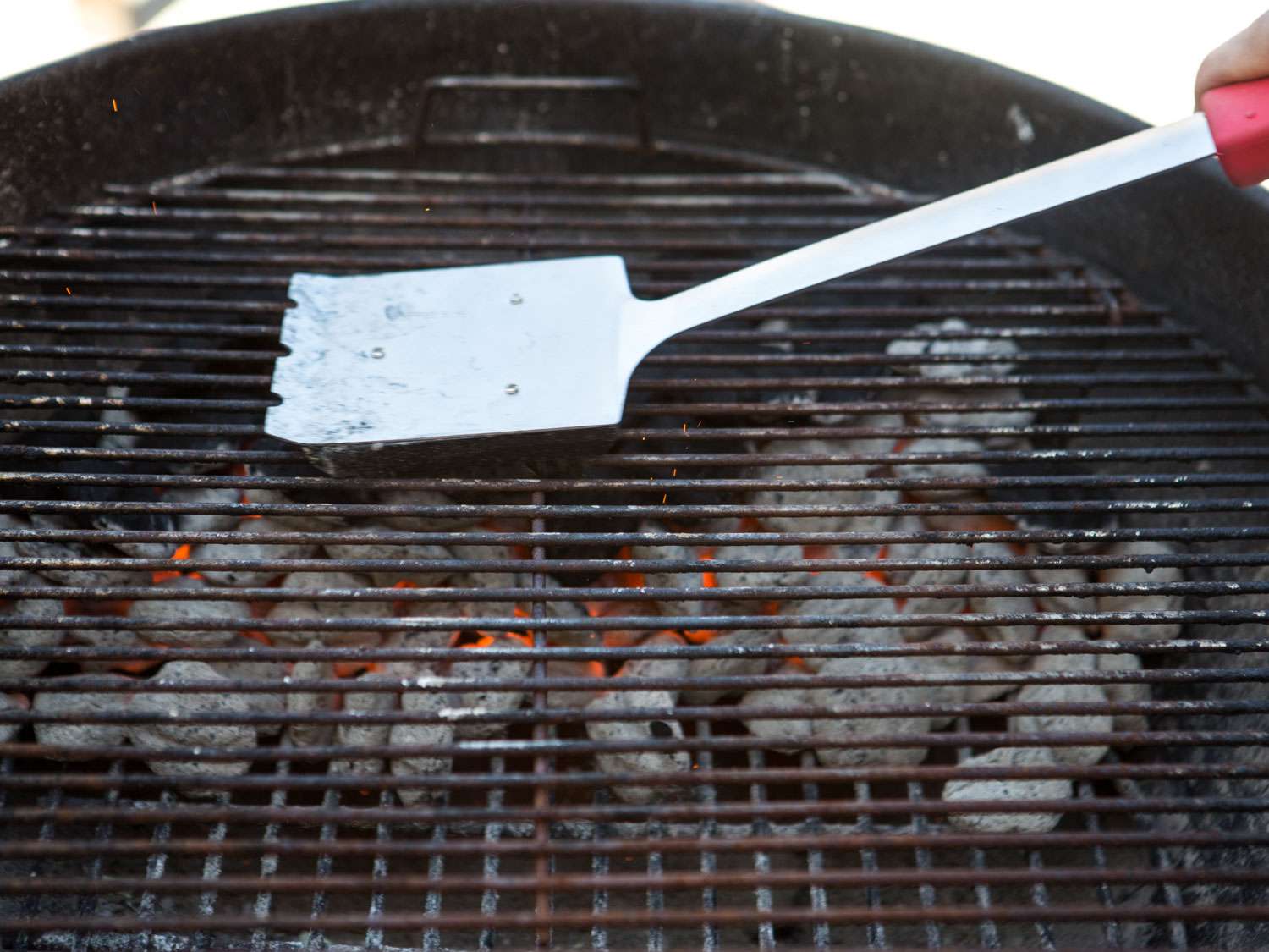Cleaning a hot grill with a grill brush.