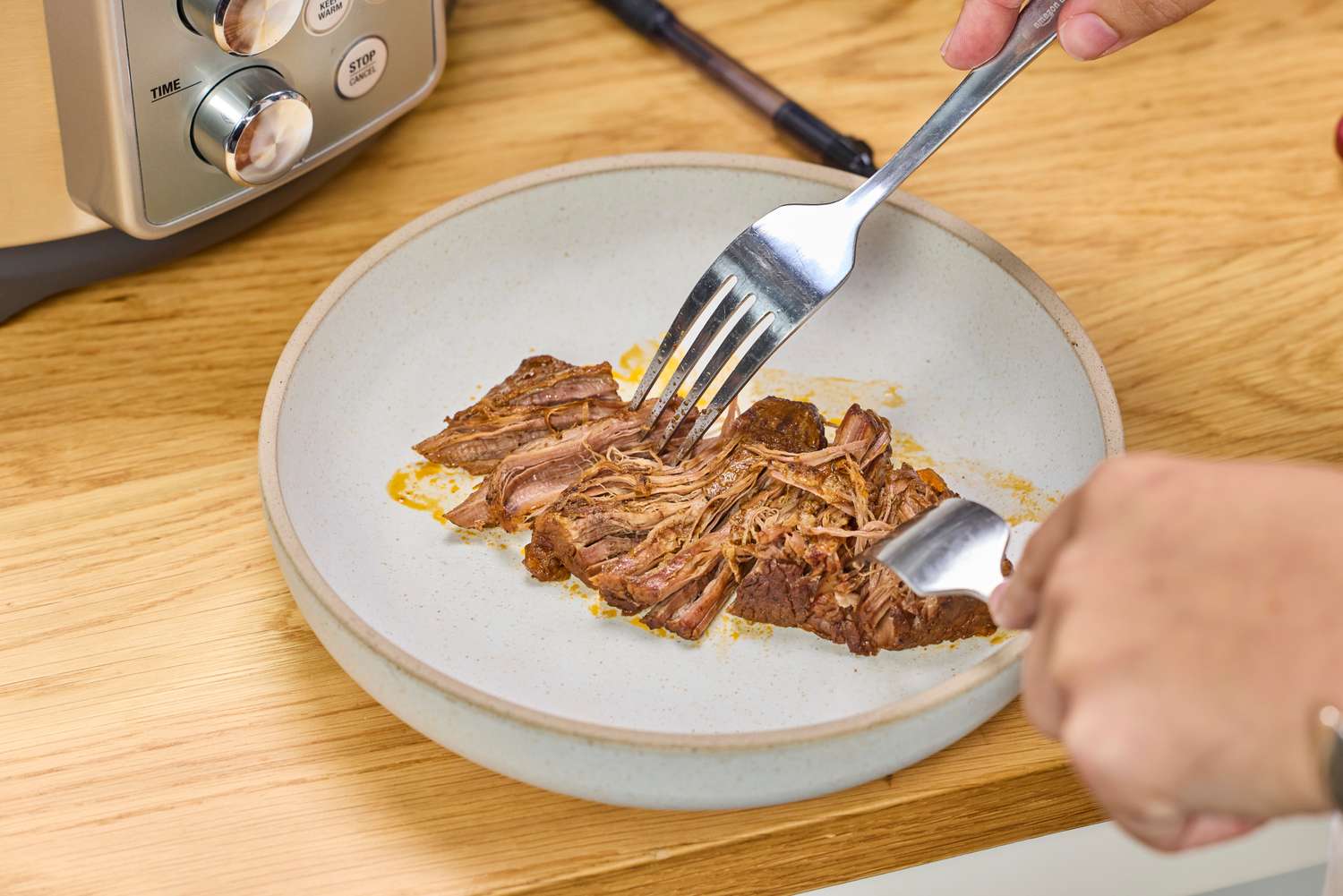 A person shreds meat cooked in the Breville the Fast Slow Pro