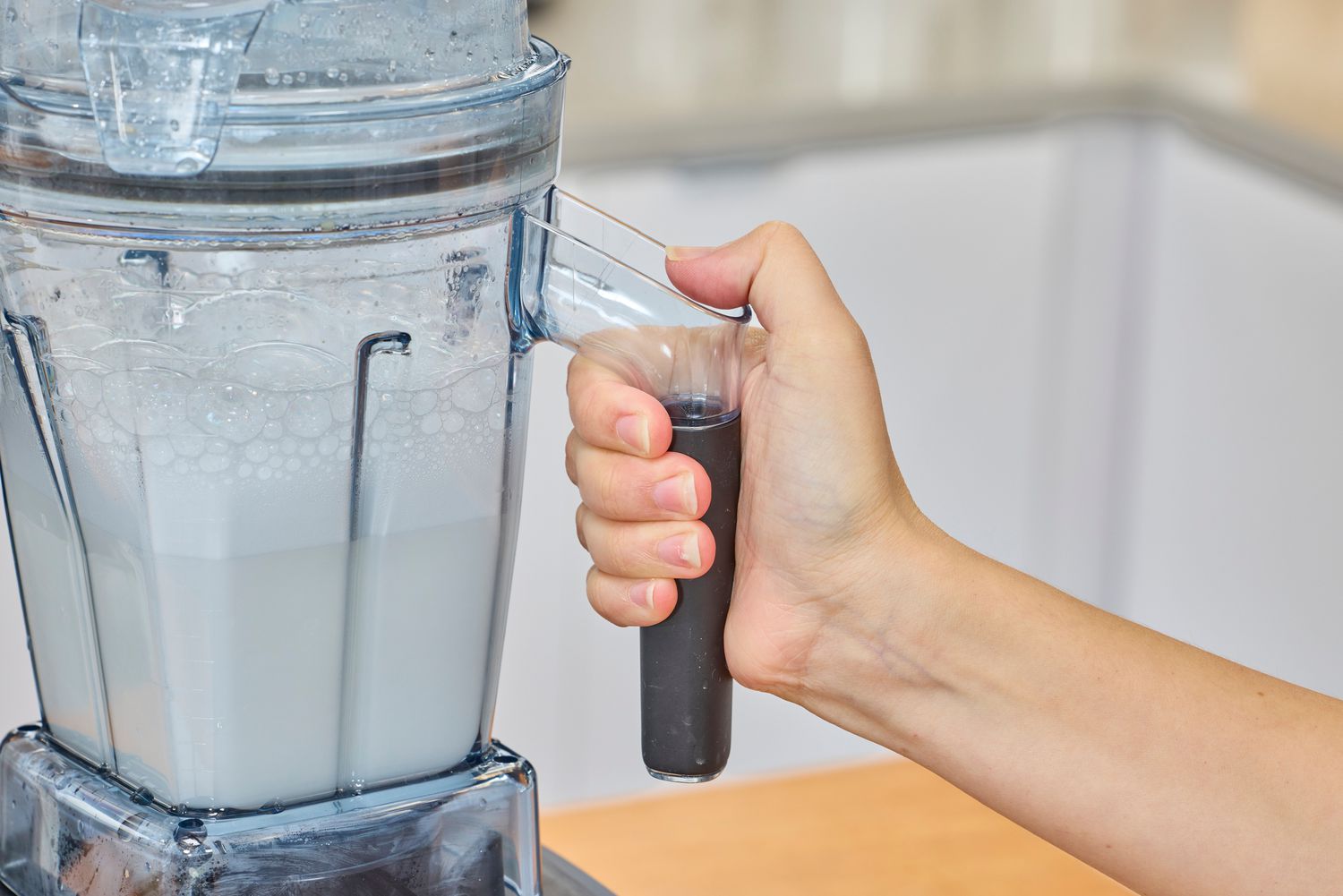 A hand holding the handle of the Vitamix Ascent X5 Blender