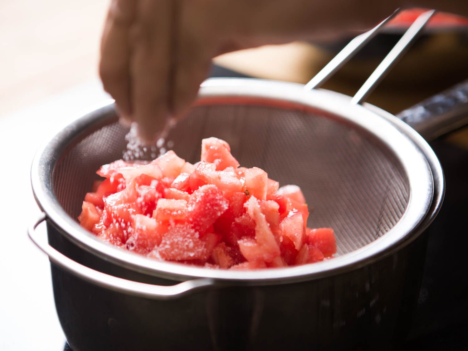 Salting diced tomatoes in a sieve.