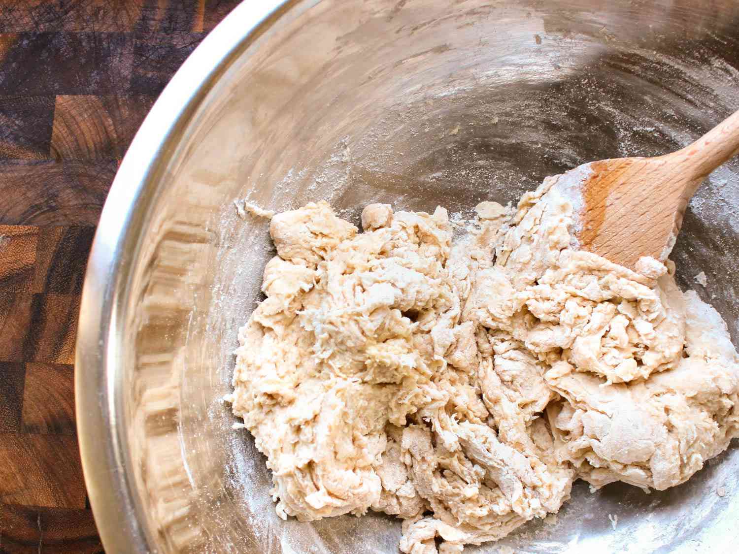 A shaggy mass of pita dough in a bowl being stirred with a wooden spoon.