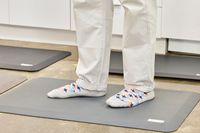 A person stands on the WellnessMats Original Anti-Fatigue Floor Mat in socks