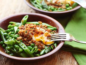 Spring vegetable salad with poached egg and crispy bread crumbs, served in a wooden bowl.