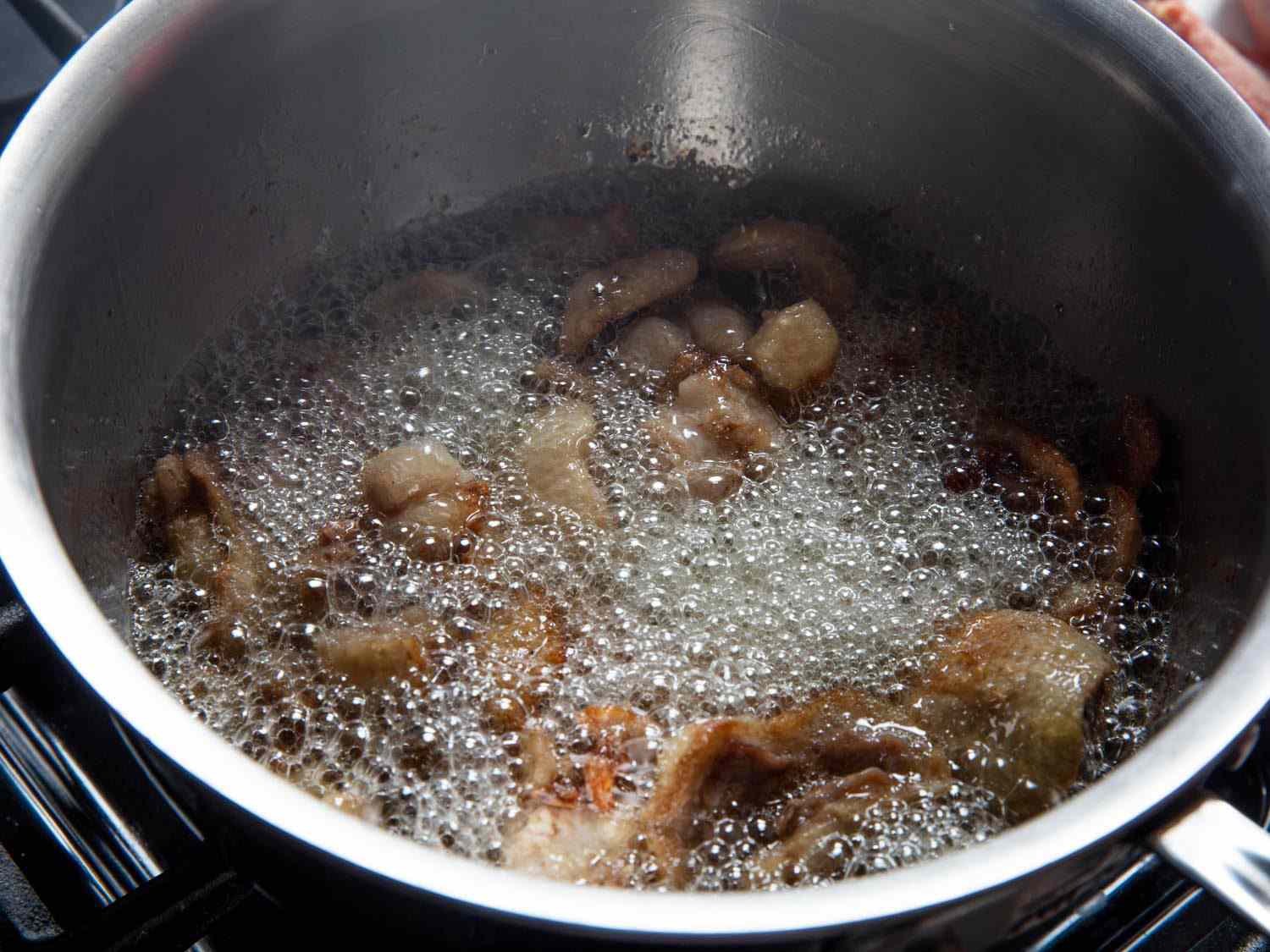 Side view of duck fat rapidly bubbling in a saucepan.