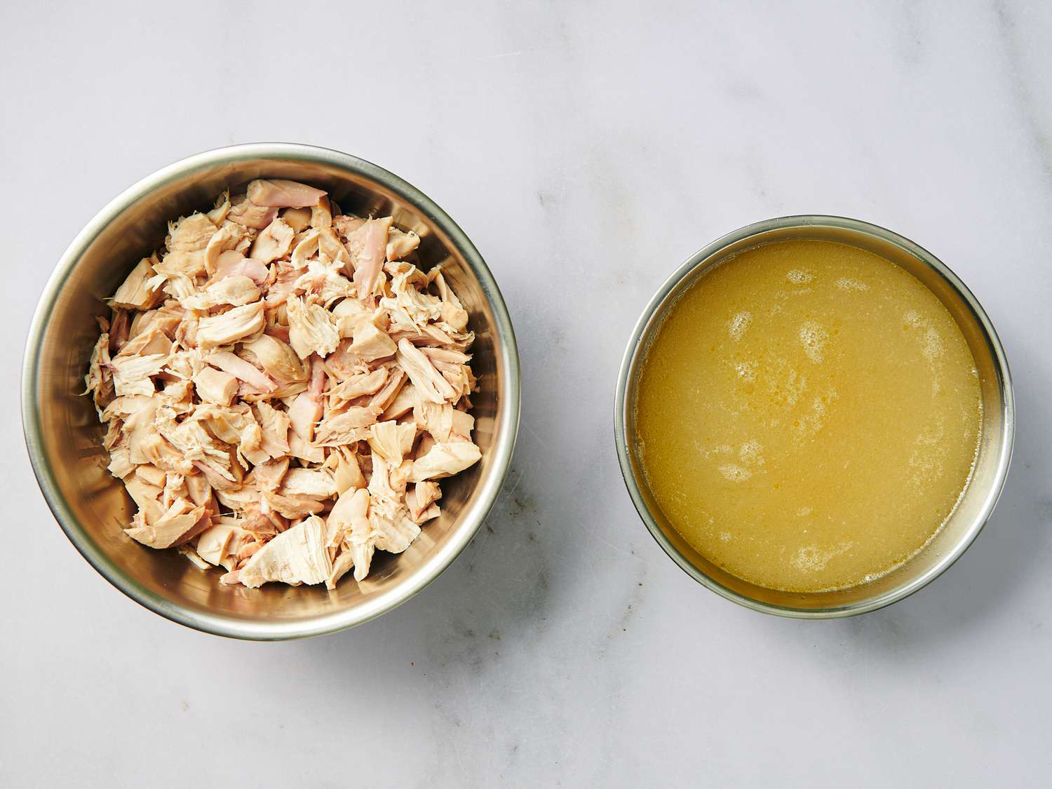 Shredded chicken in a bowl and strained broth in a separate smaller bowl, side by side.