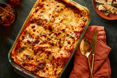 A baked lasagna in a glass dish with utensils and a napkin on the side