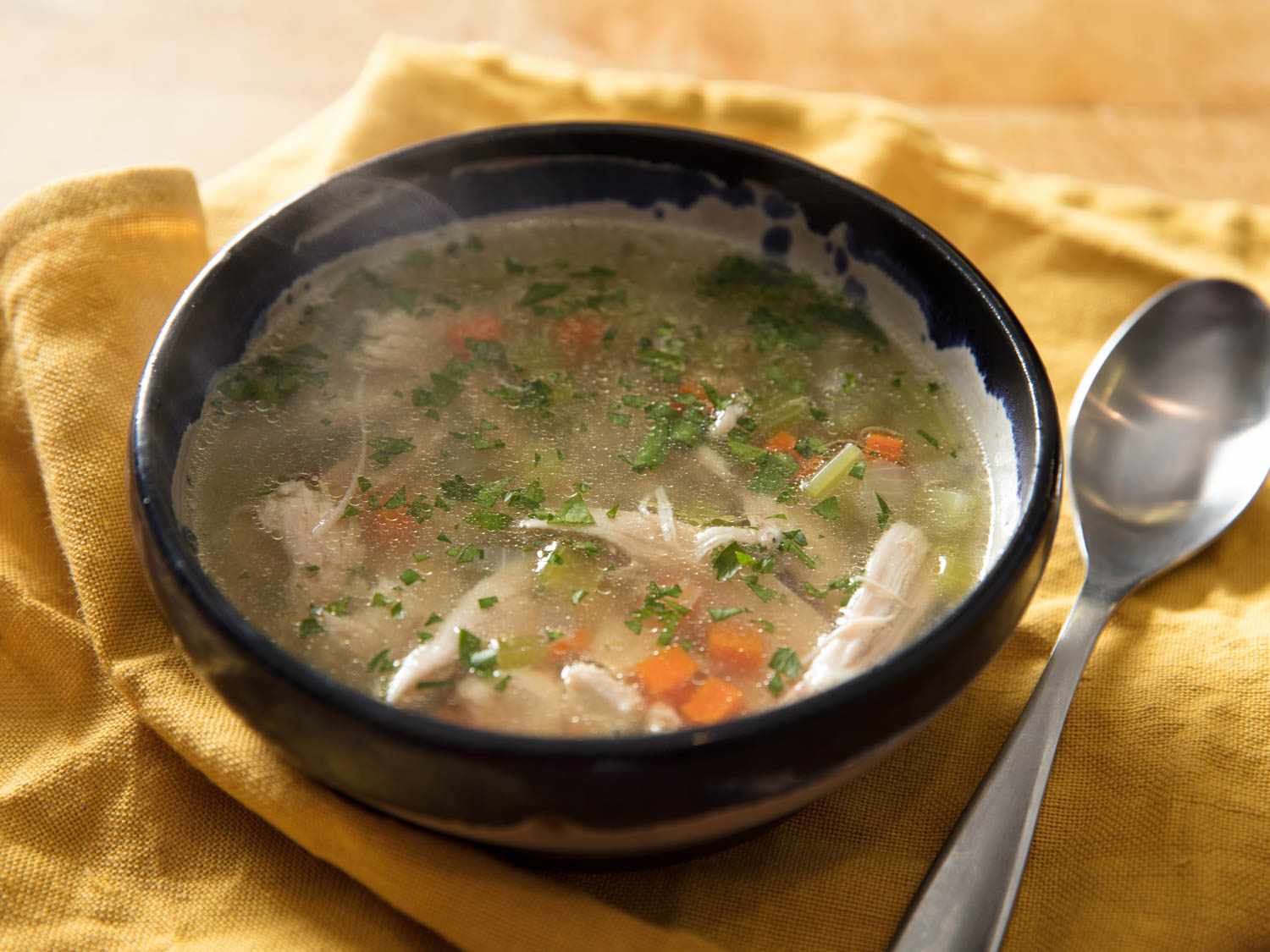 Chicken soup, served steaming in a ceramic bowl.