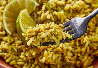 A fork holding a portion of seasoned rice with lime slices in the background