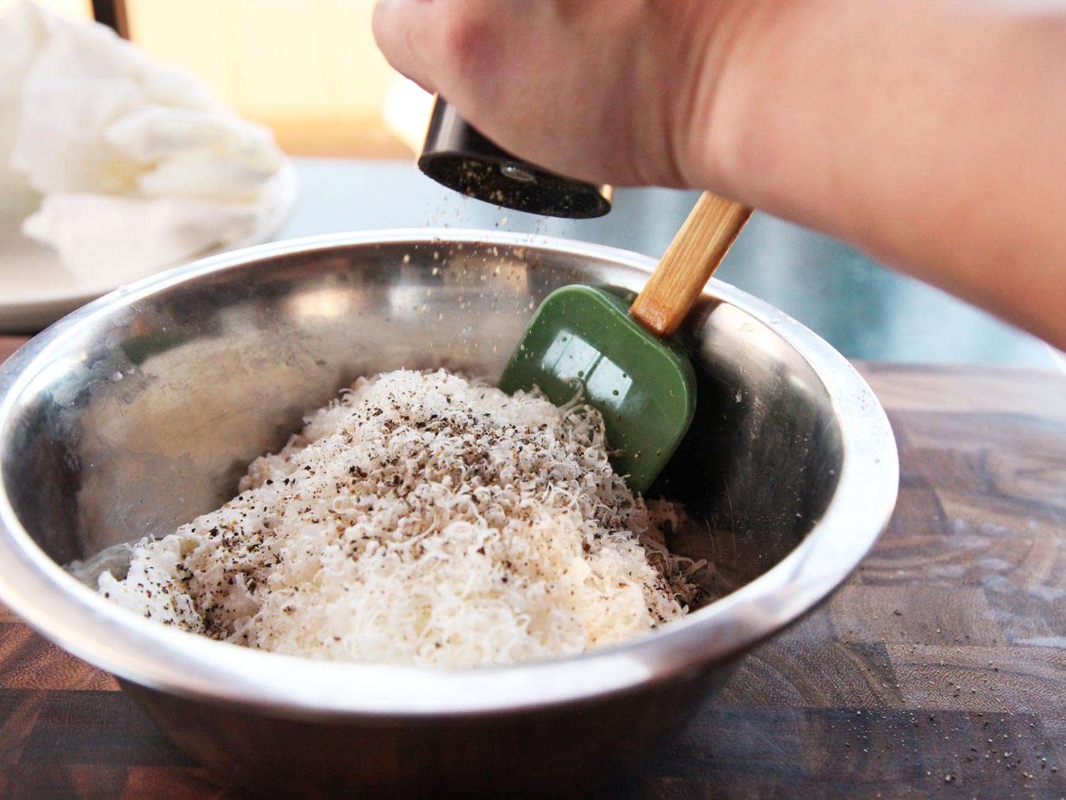 Ricotta and grated Parmesan in a mixing bowl, sprinkled with ground black pepper. 
