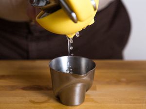 Juice being squeeze from a lemon into a small metal measuring cup.