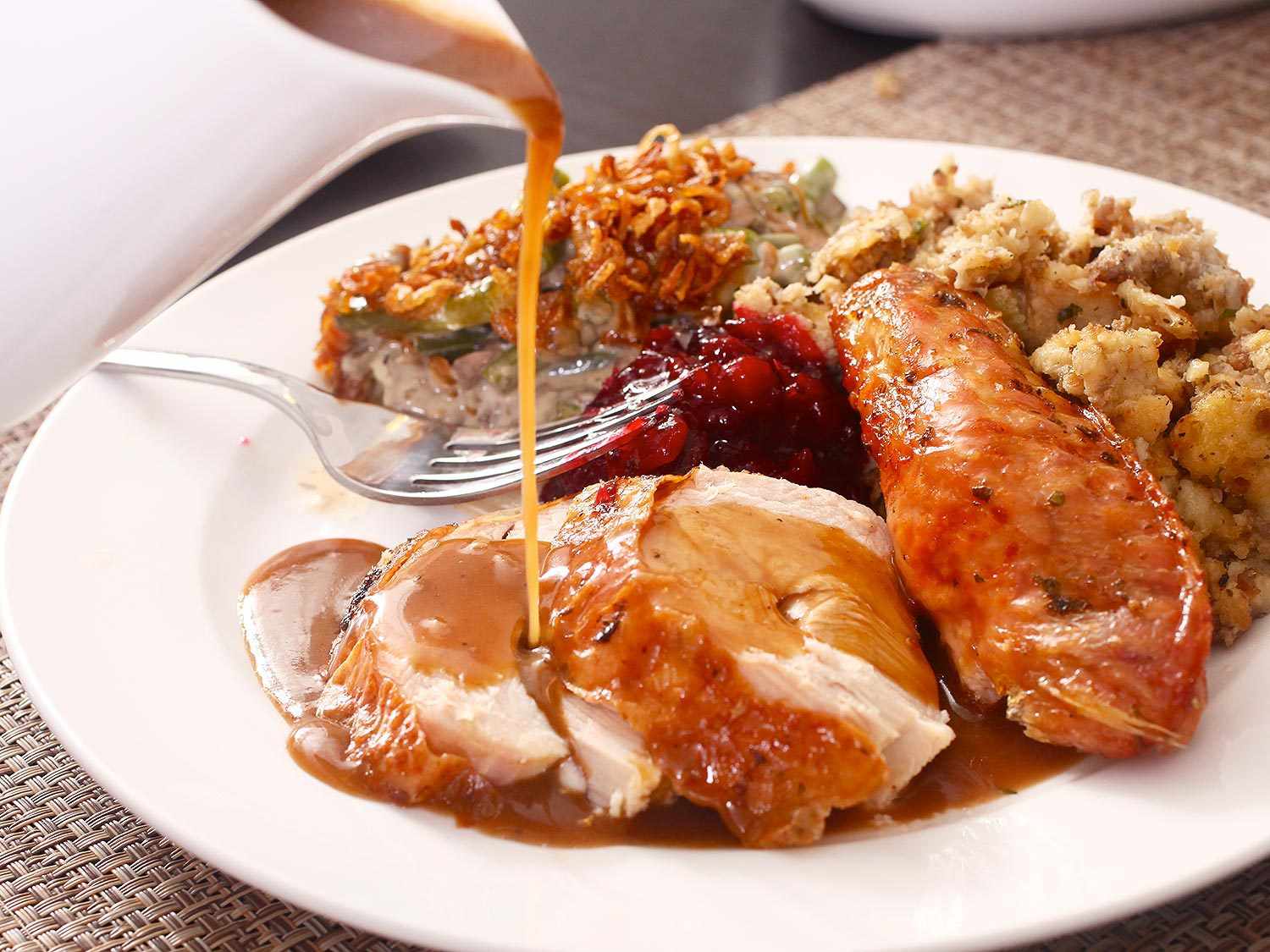 Pouring gravy over a serving plate of turkey and sides.