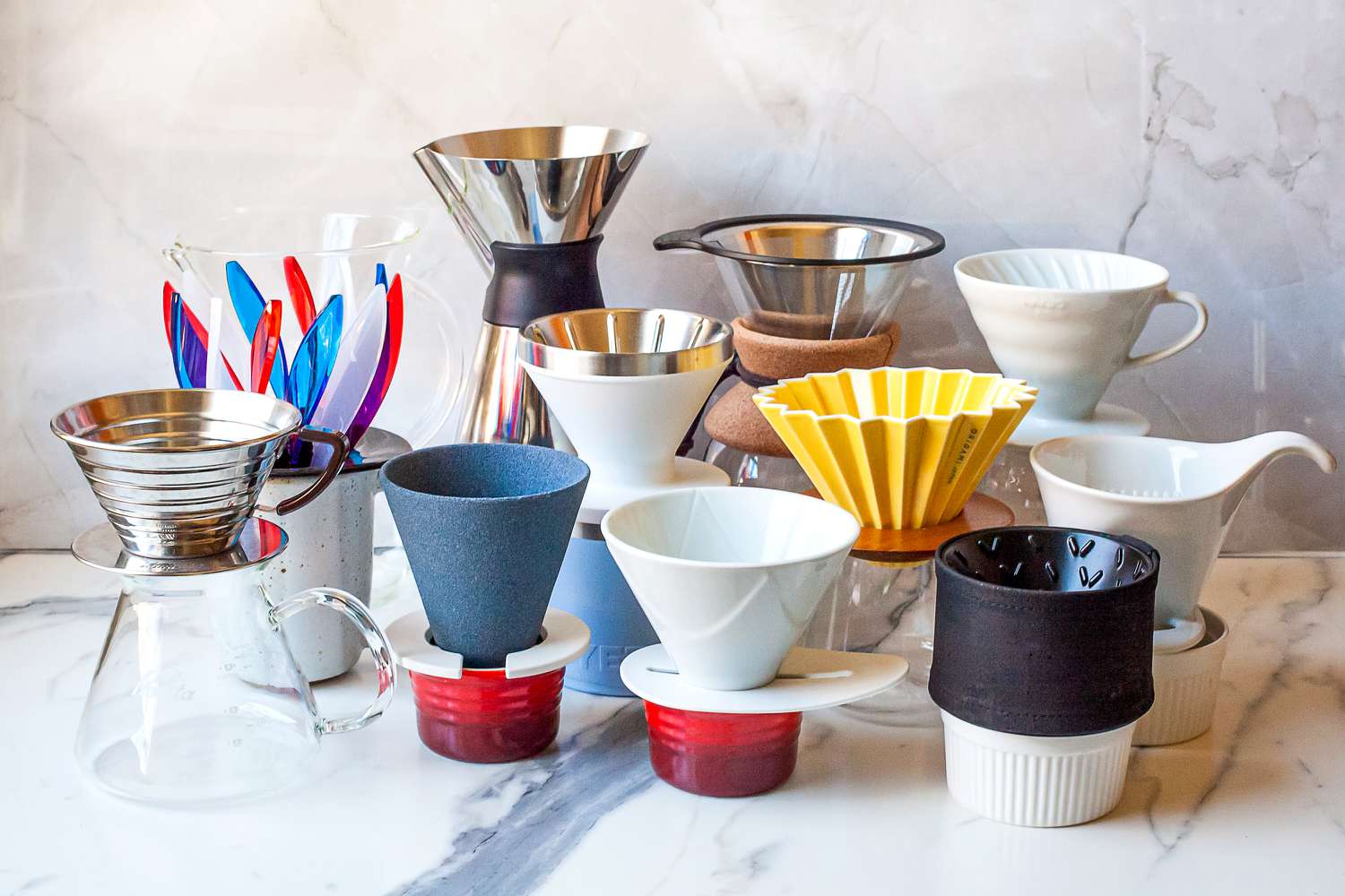 Various pour-over coffee drippers arranged on a marble surface, showcasing different designs and materials