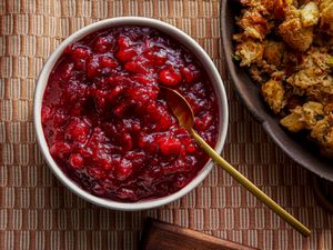 Finished cranberry sauce in a small bowl next to a bowl of stuffing with a gold spoon