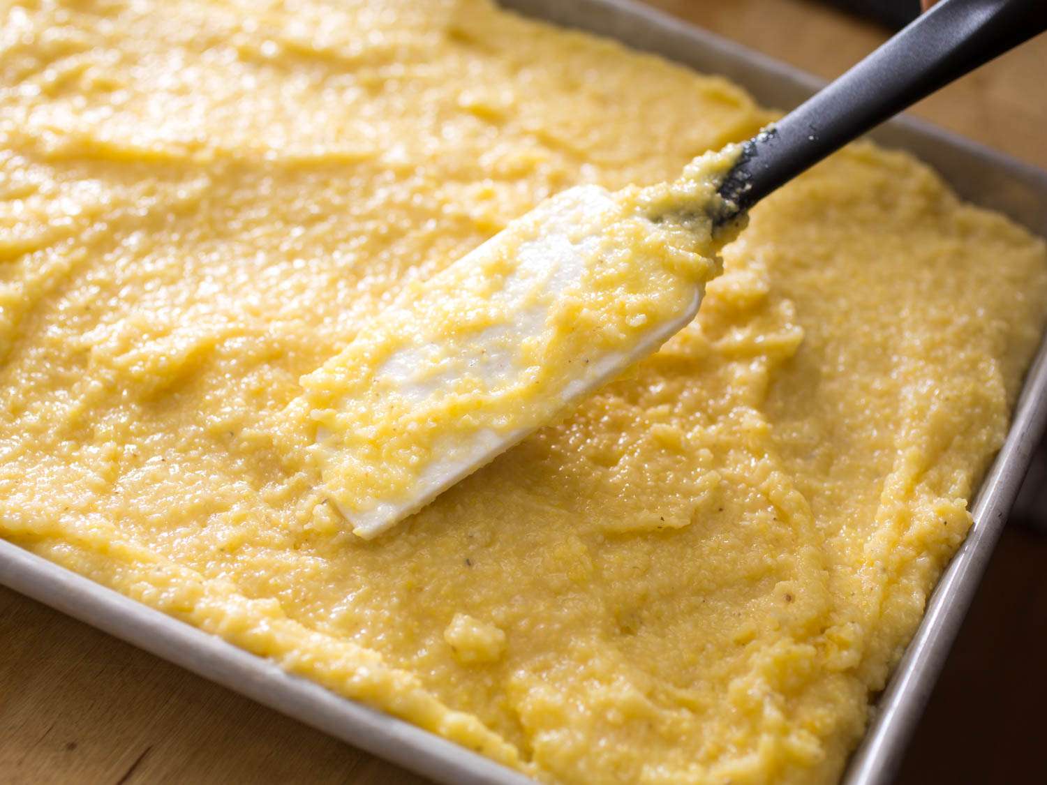 Evenly spreading polenta across a rimmed baking sheet.