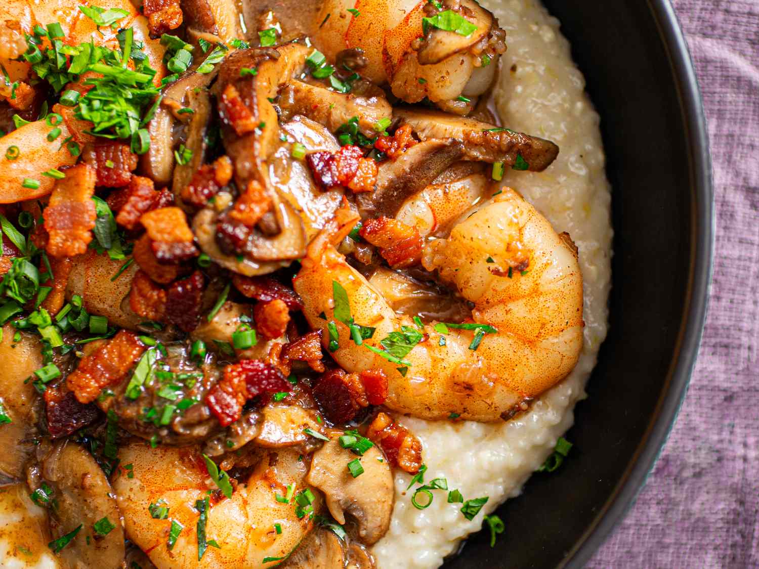 A dish featuring shrimp diced bacon mushrooms and garnish over a creamy base served in a bowl
