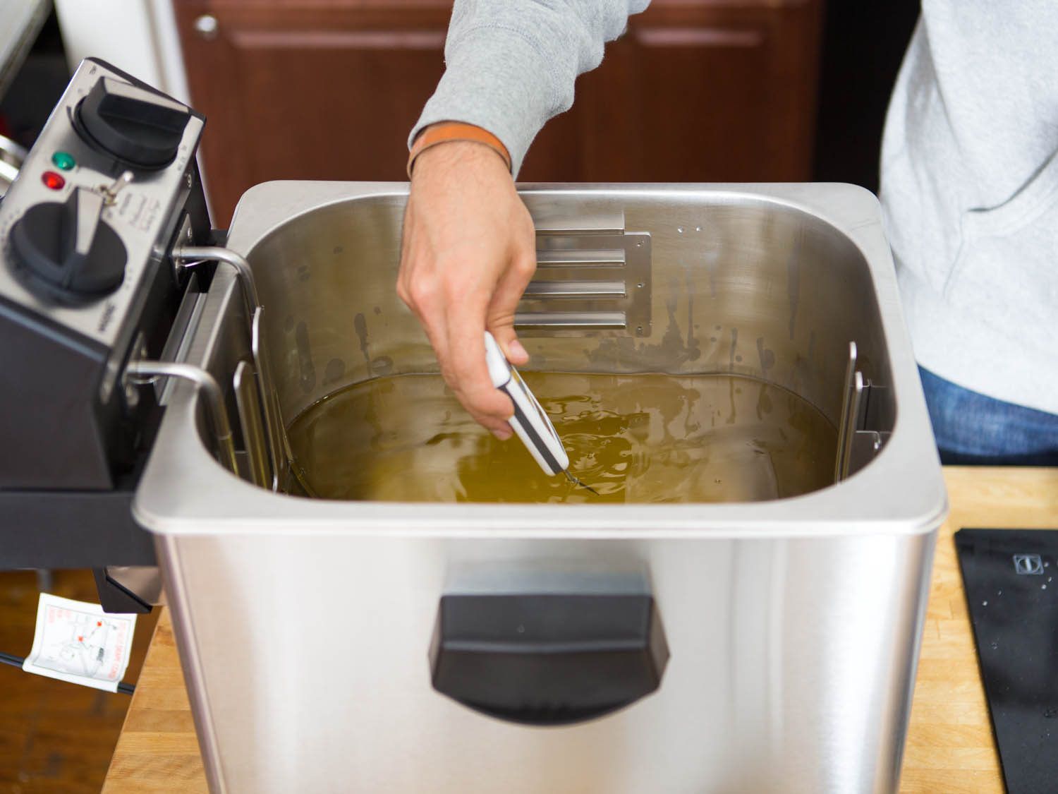 Checking temperature of indoor deep fryer with thermometer.