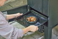 A person places wood chips into the Cuisinart COS-244 Vertical 36-inch Propane Smoker