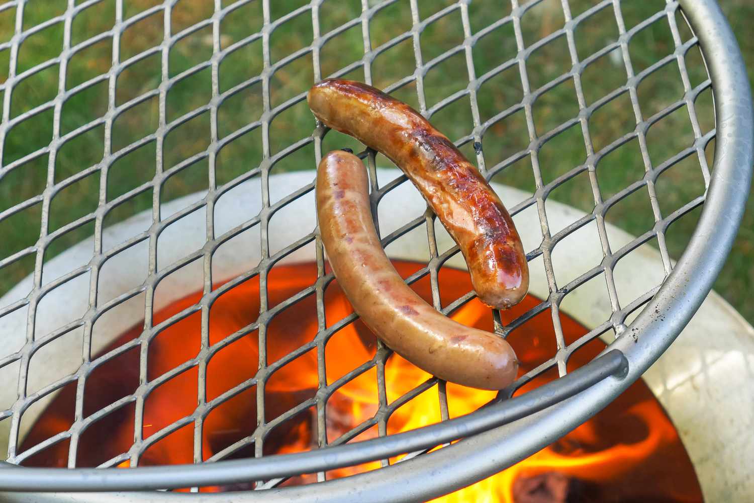 Two hot dogs grilling over a flame on a metal grill