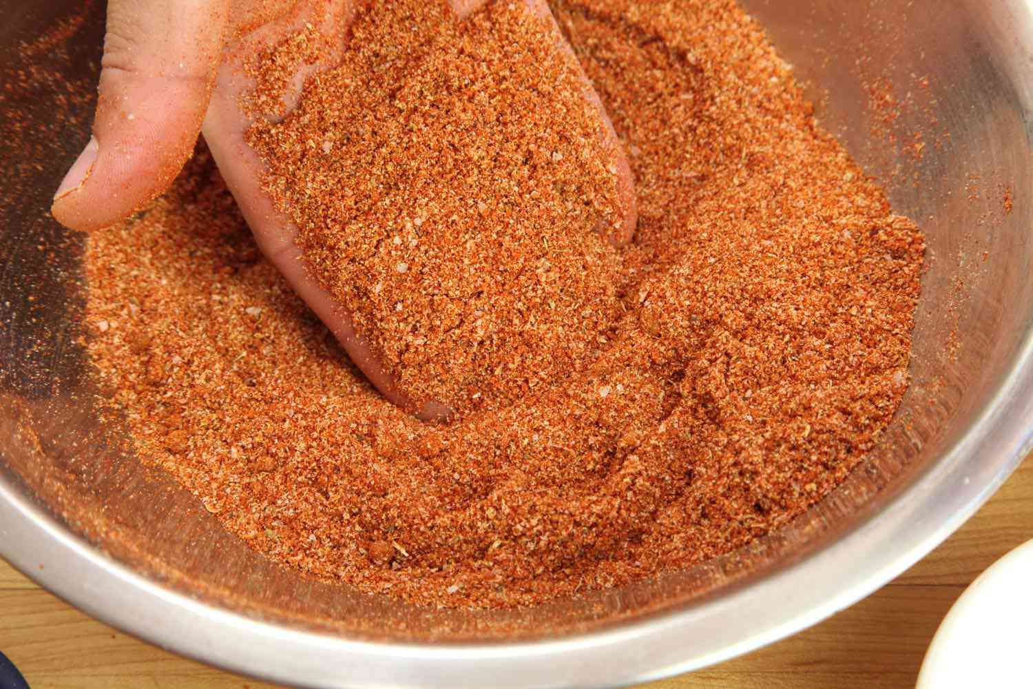 A stainless steel bowl full of spices for the rib rub, and a hand picking up a palmful.