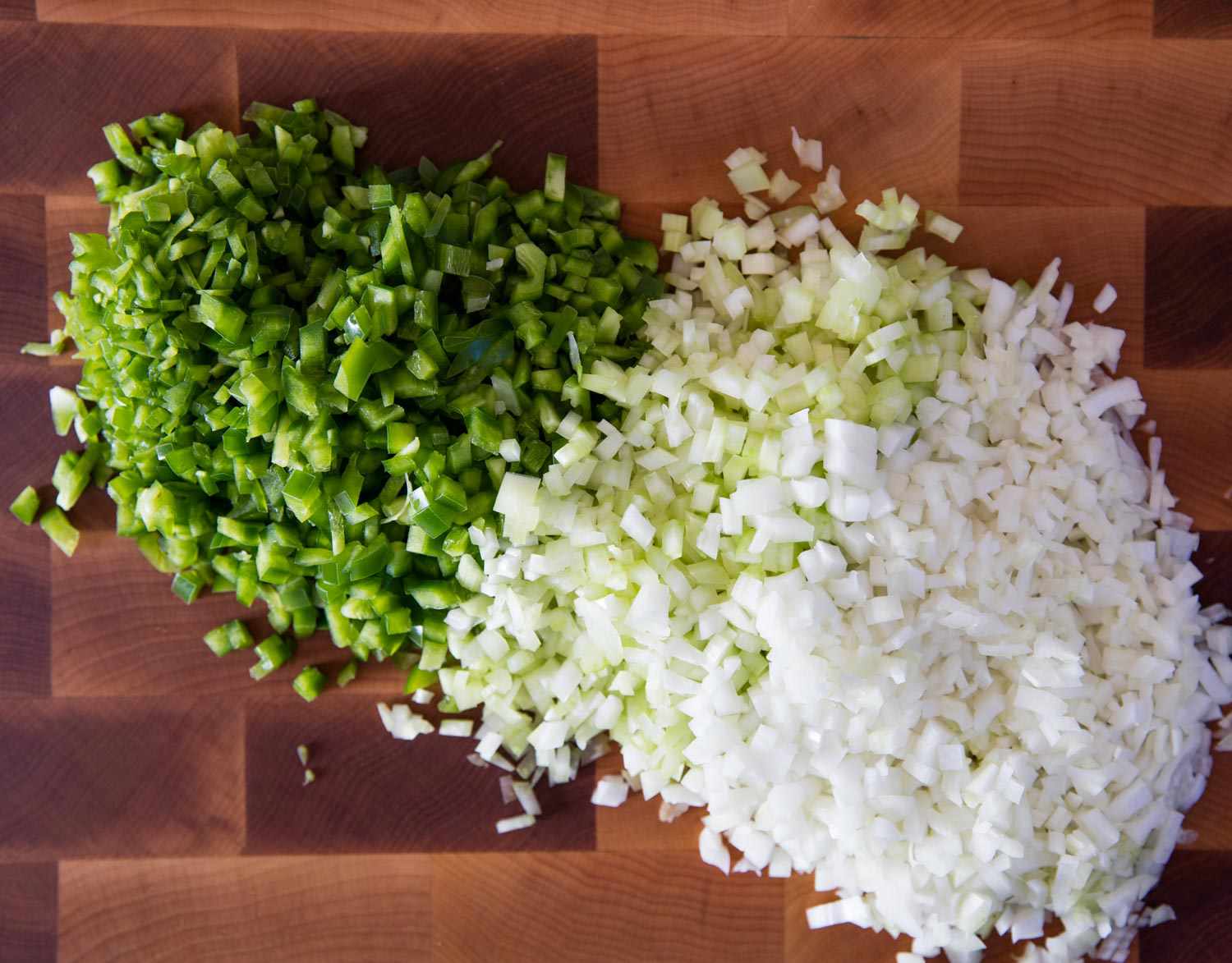 Overhead close-up of piles of diced celery, green pepper, and onion on a cutting board.