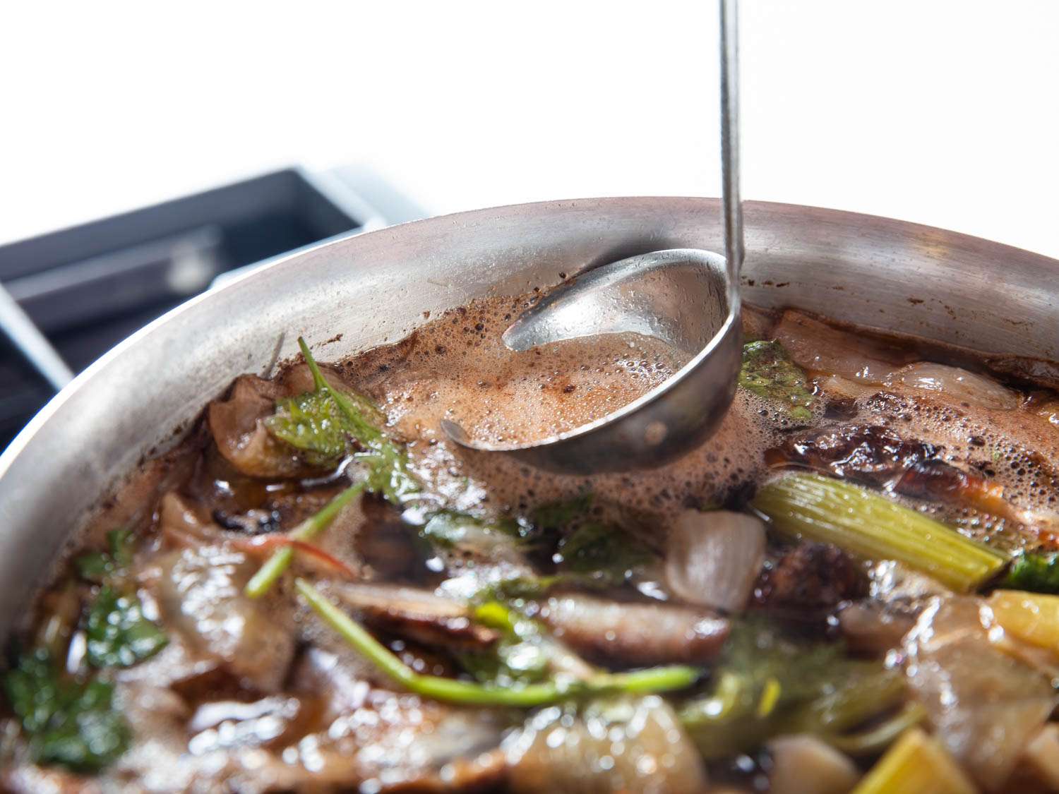 A ladle skimming the surface of the duck stock pot. 