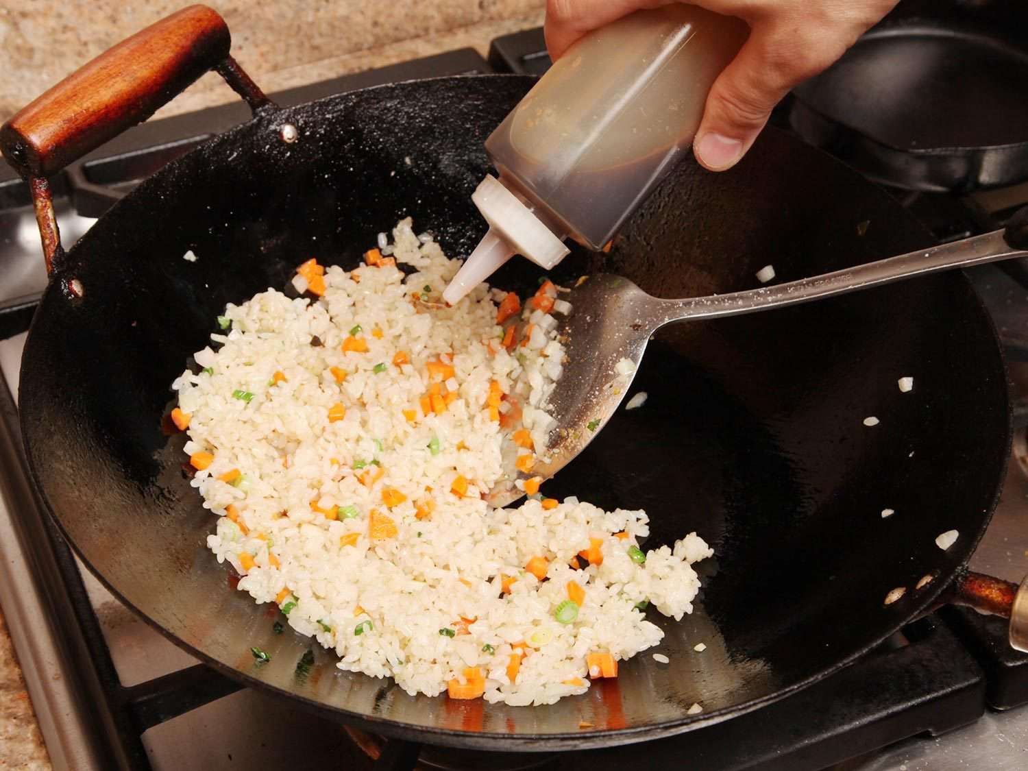 Adding soy sauce to fried rice in a wok.