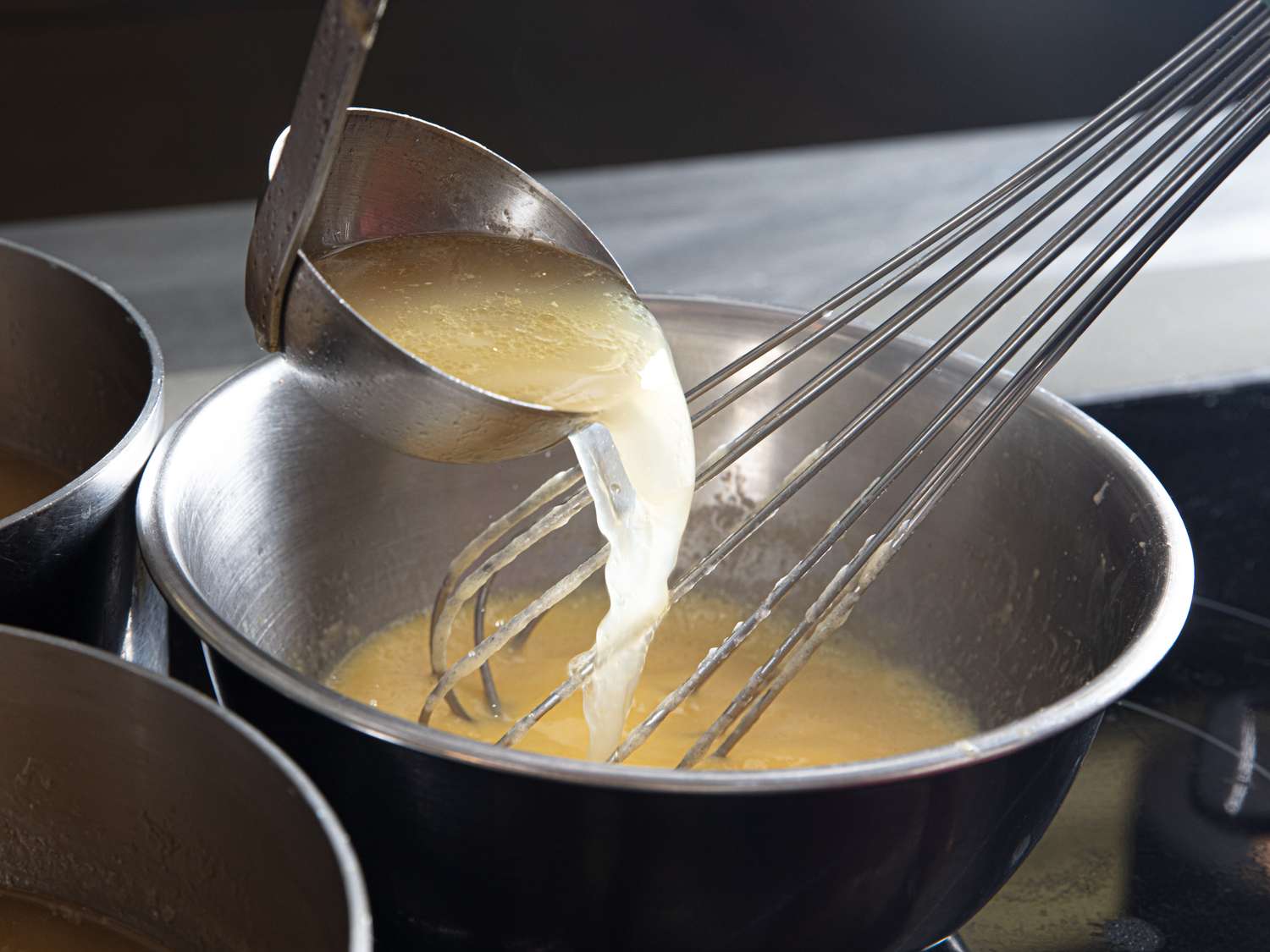 A ladle pouring soup into a mixing bowl with a whisk placed inside