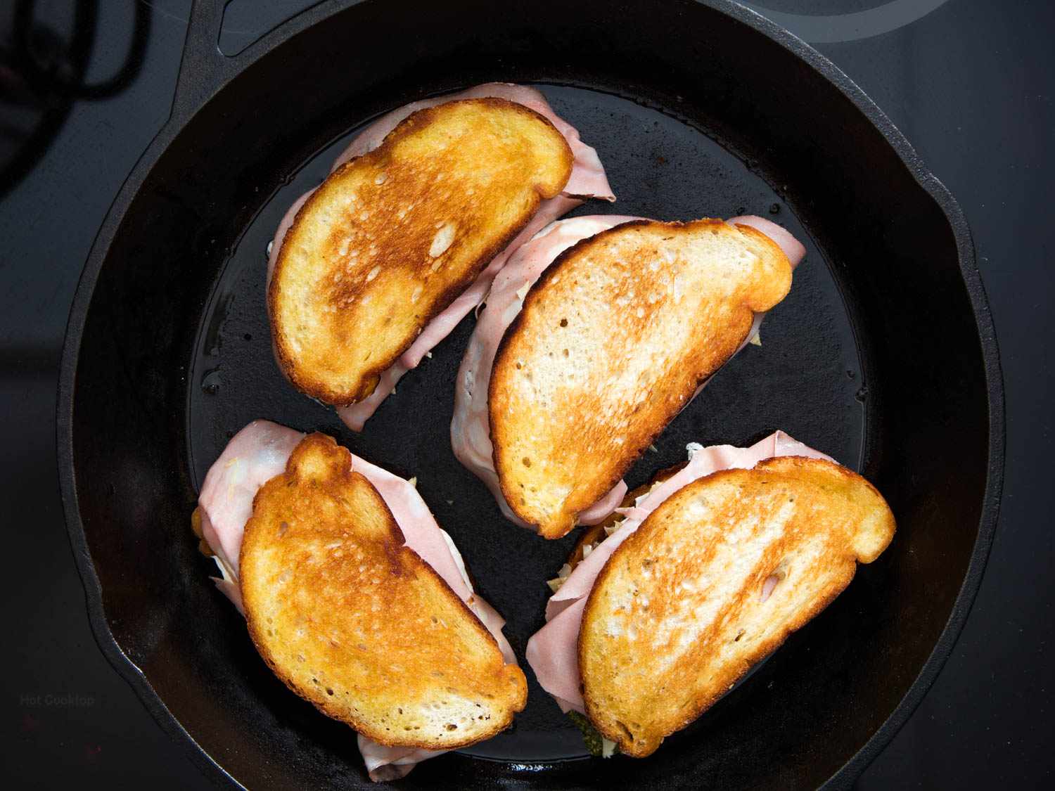Overhead view of the assembled sandwiches in a cast iron skillet, ready to pop in the oven.