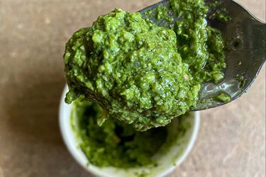 A spoonful of pesto with a container underneath