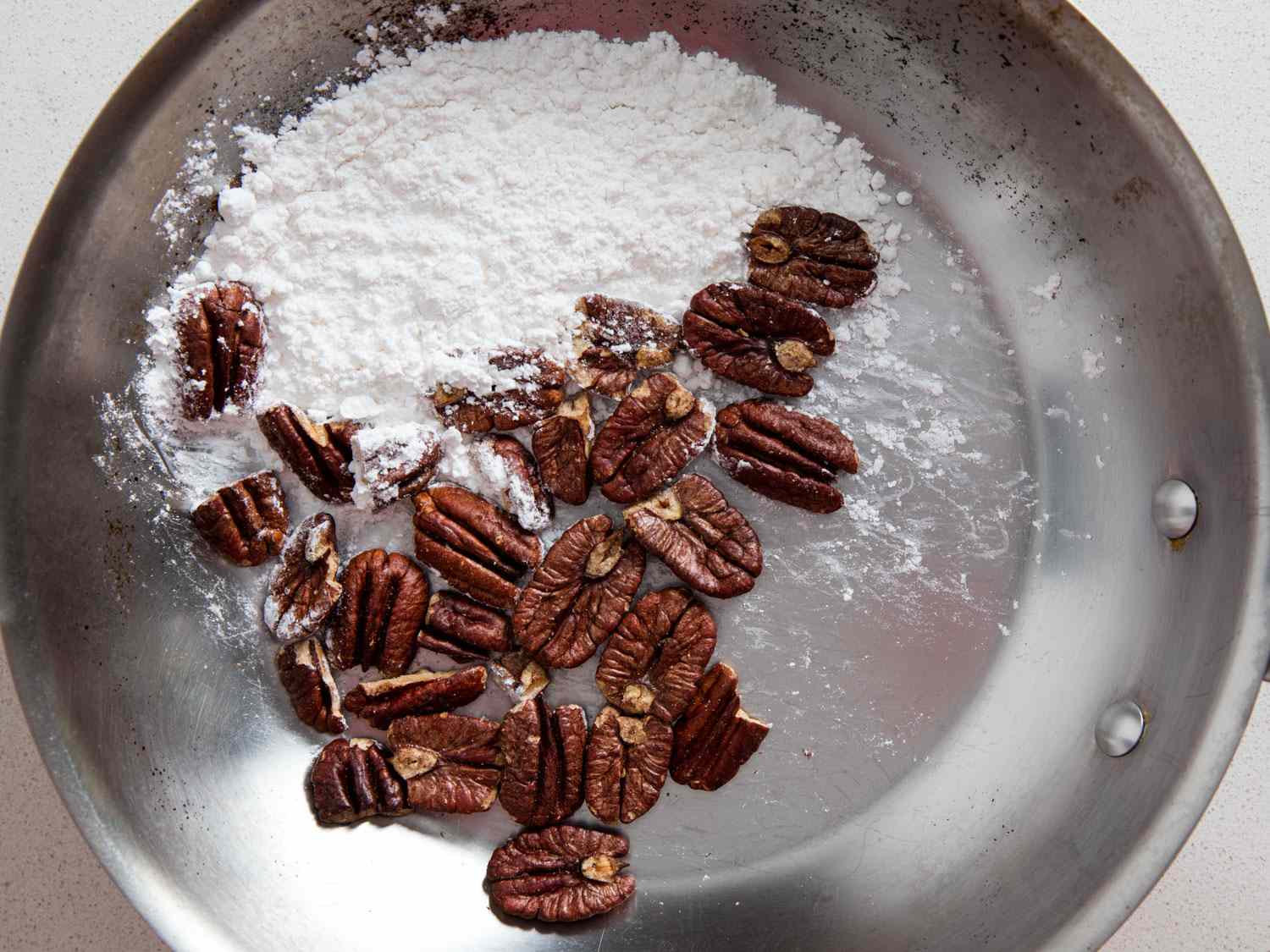 Overhead view of the pecans and powdered sugar in a skillet, freshly toasted. The pecans are significantly darker.