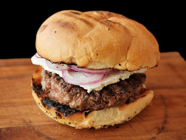 A lamb burger, served on a grilled bun with a slice of feta and redo onions.