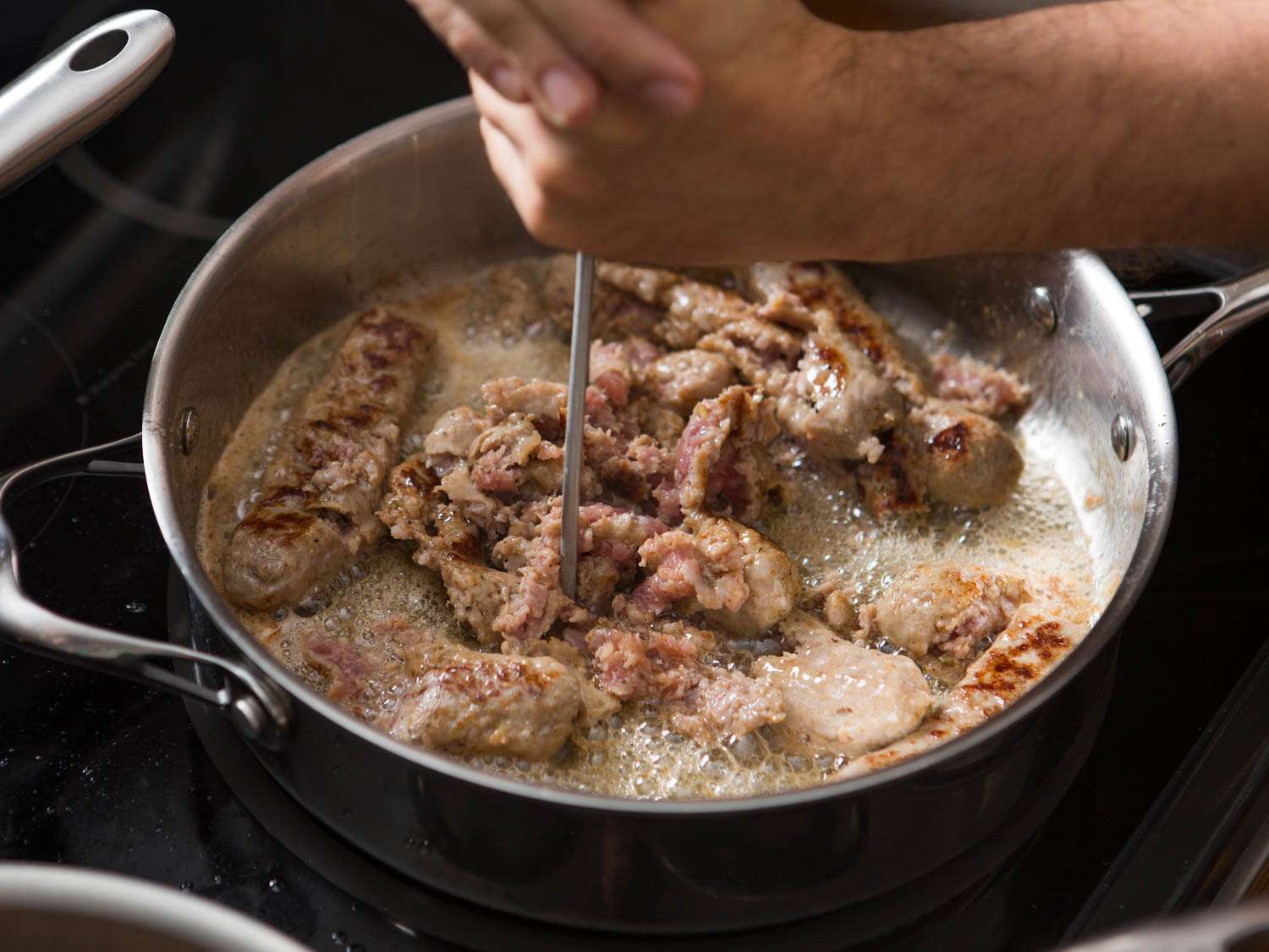 Breaking up sausage in a skillet with a potato smasher. 