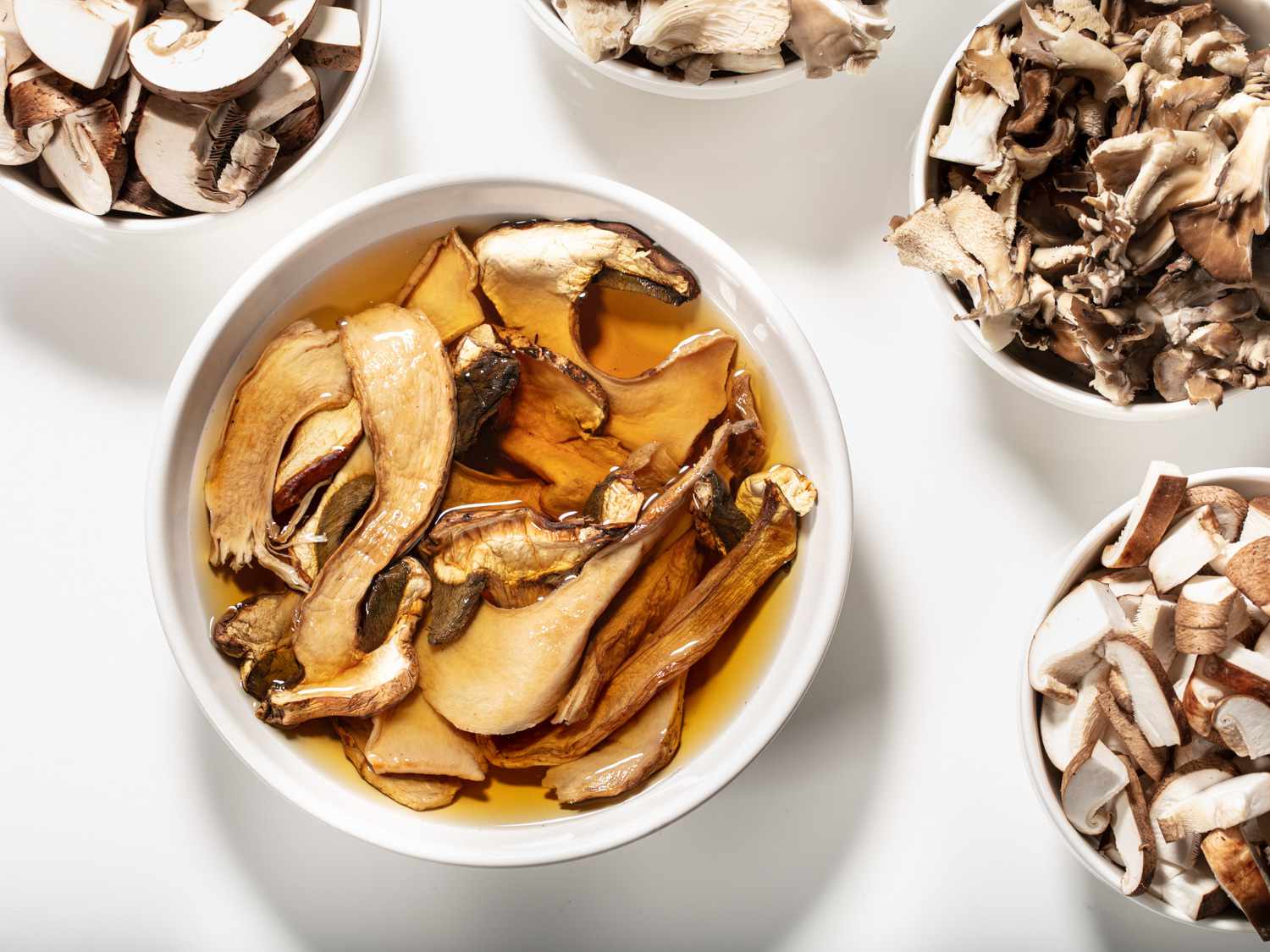 Bowls of mushrooms, with the largest bowl holding mushrooms rehydrating in water.