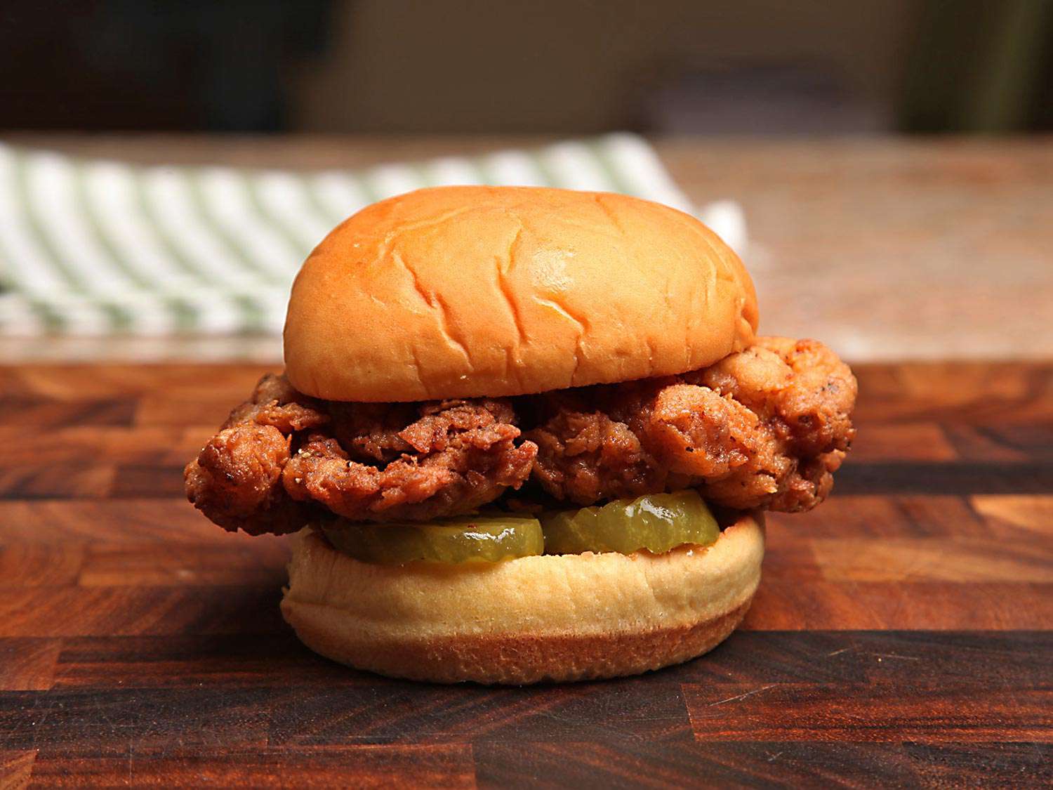 Fried chicken sandwich on a wooden cutting board.