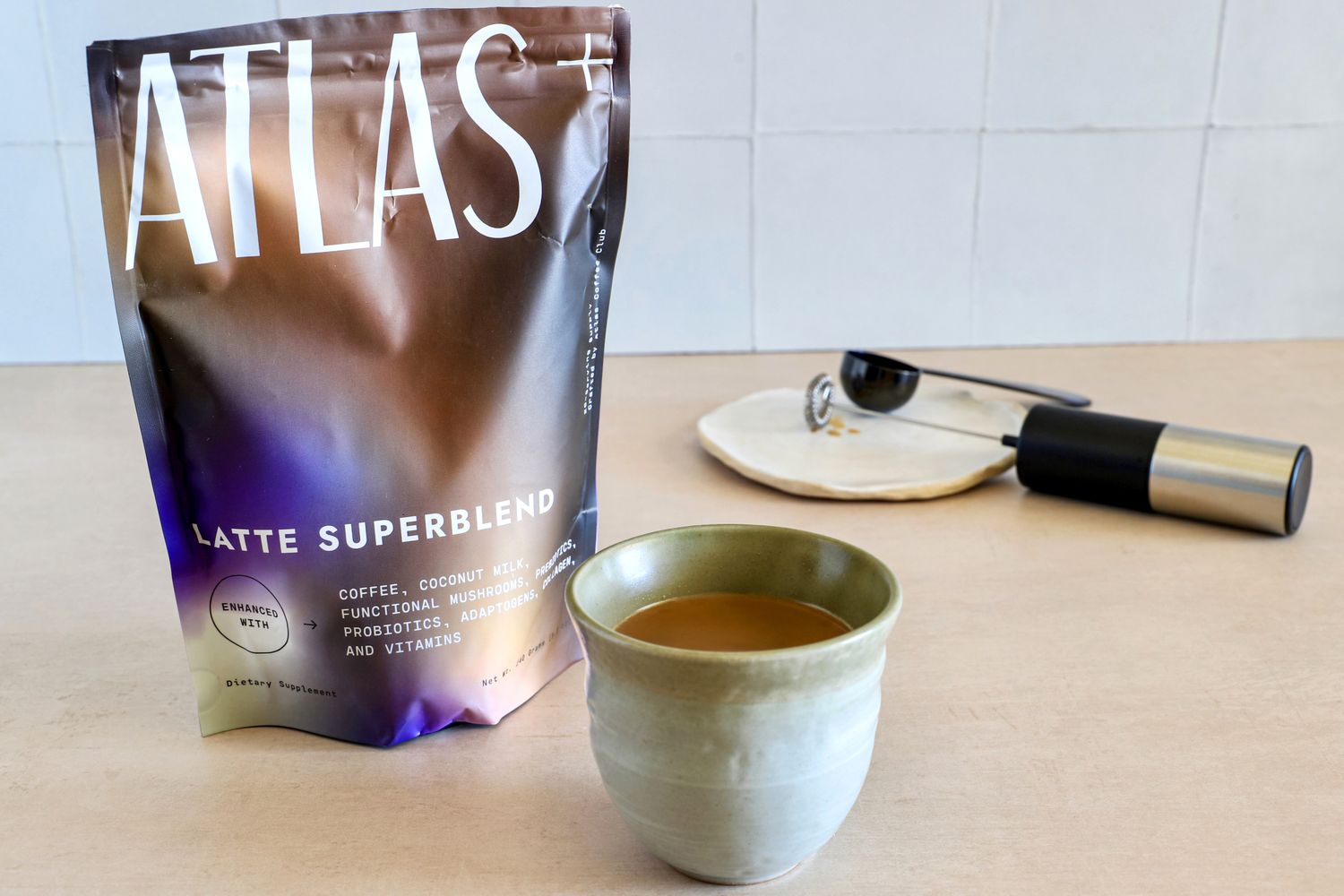 A package of Atlas Latte Superblend mushroom coffee mix along with a cup of the prepared latte and a handheld milk frother.