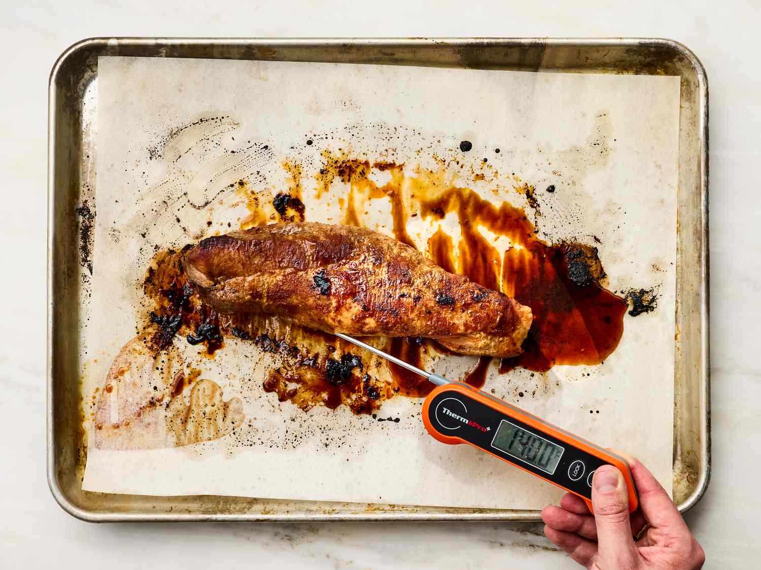 Roasted pork tenderloin on a baking sheet with a thermometer checking its internal temperature