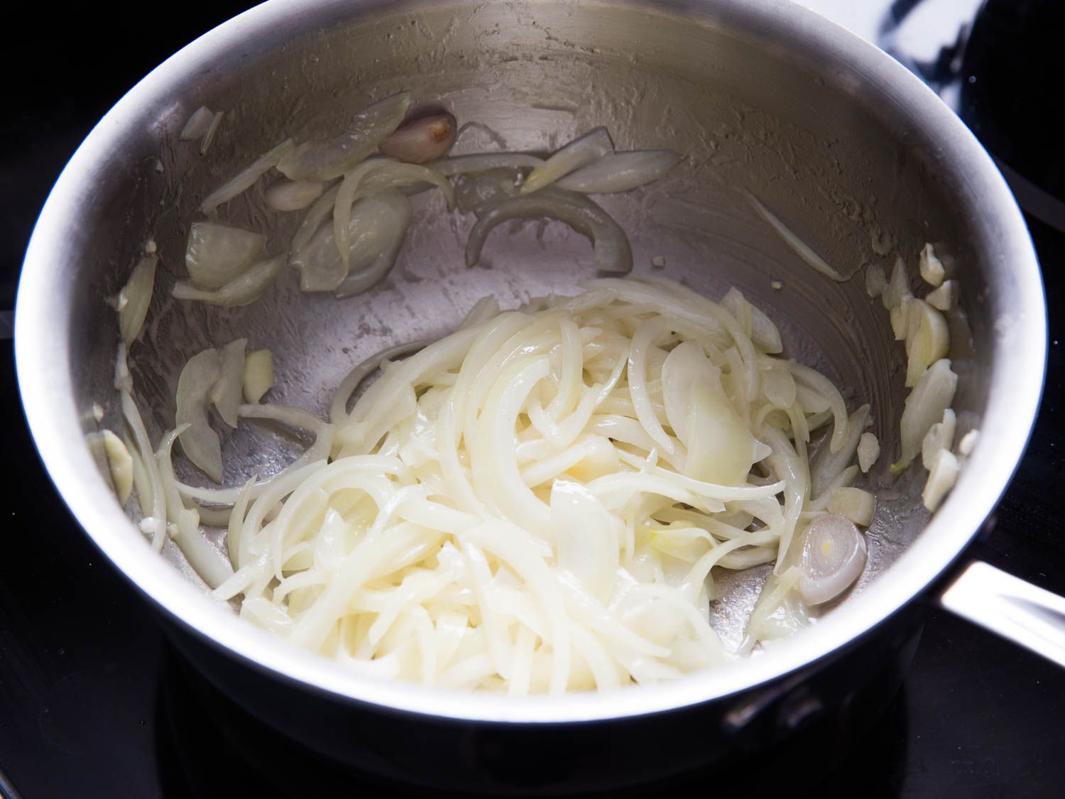Sliced onion and garlic being gently cooked in a saucepan.