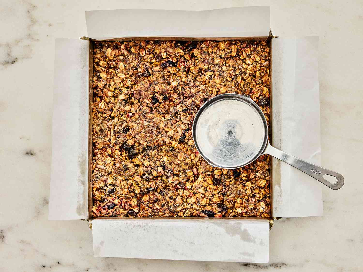 Granola mixture pressed into smaller pan with a greased measuring cup