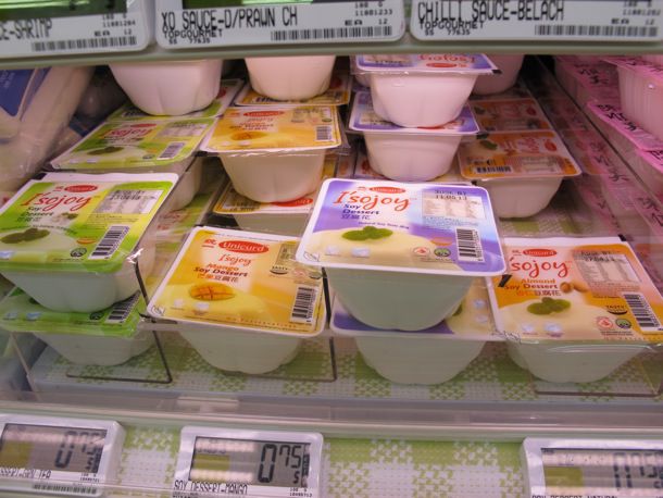 Different flavors of soya beancurd on display in the refrigerated section of a grocery store.