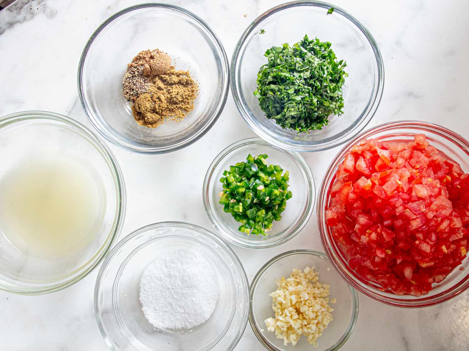 Ingredients in bowls including diced tomatoes chopped herbs spices and minced garlic