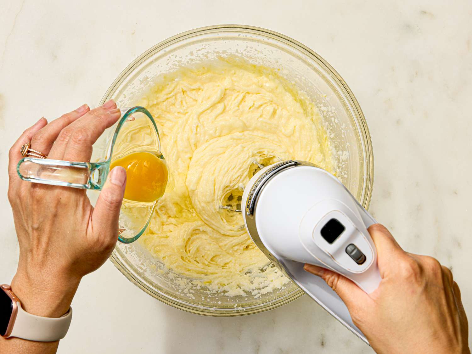 Hands adding an egg to a mixing bowl with batter using a handheld mixer