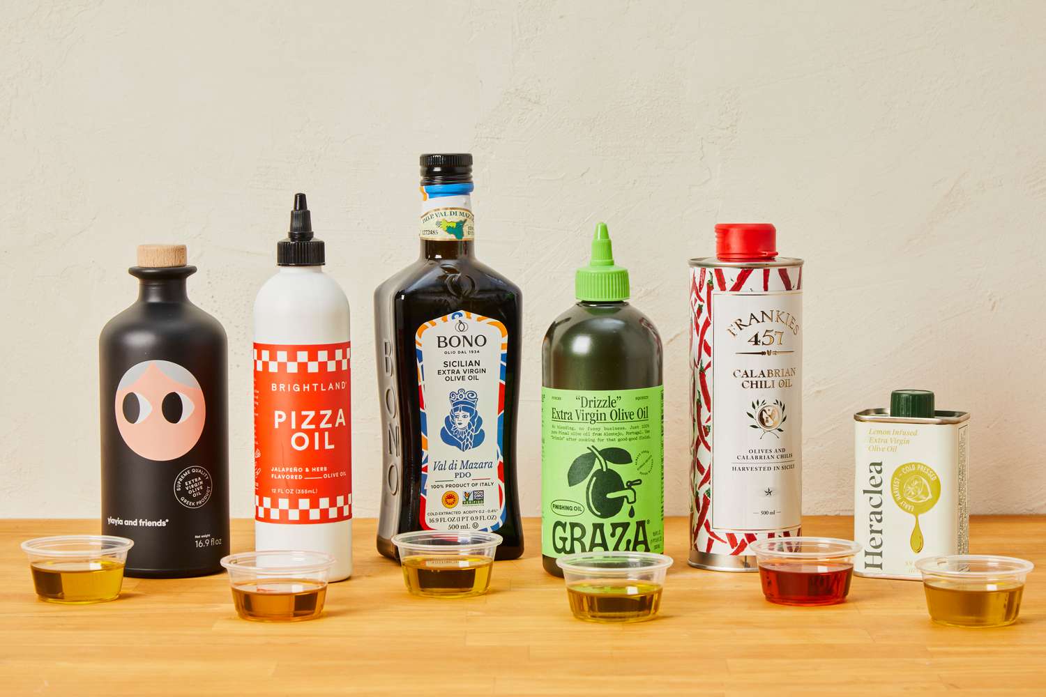 Bottles of olive oil with small cups of oil in front of the bottles.