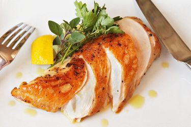 A plate with sliced sous vide chicken breast with a lemon wedge and fresh herbs.