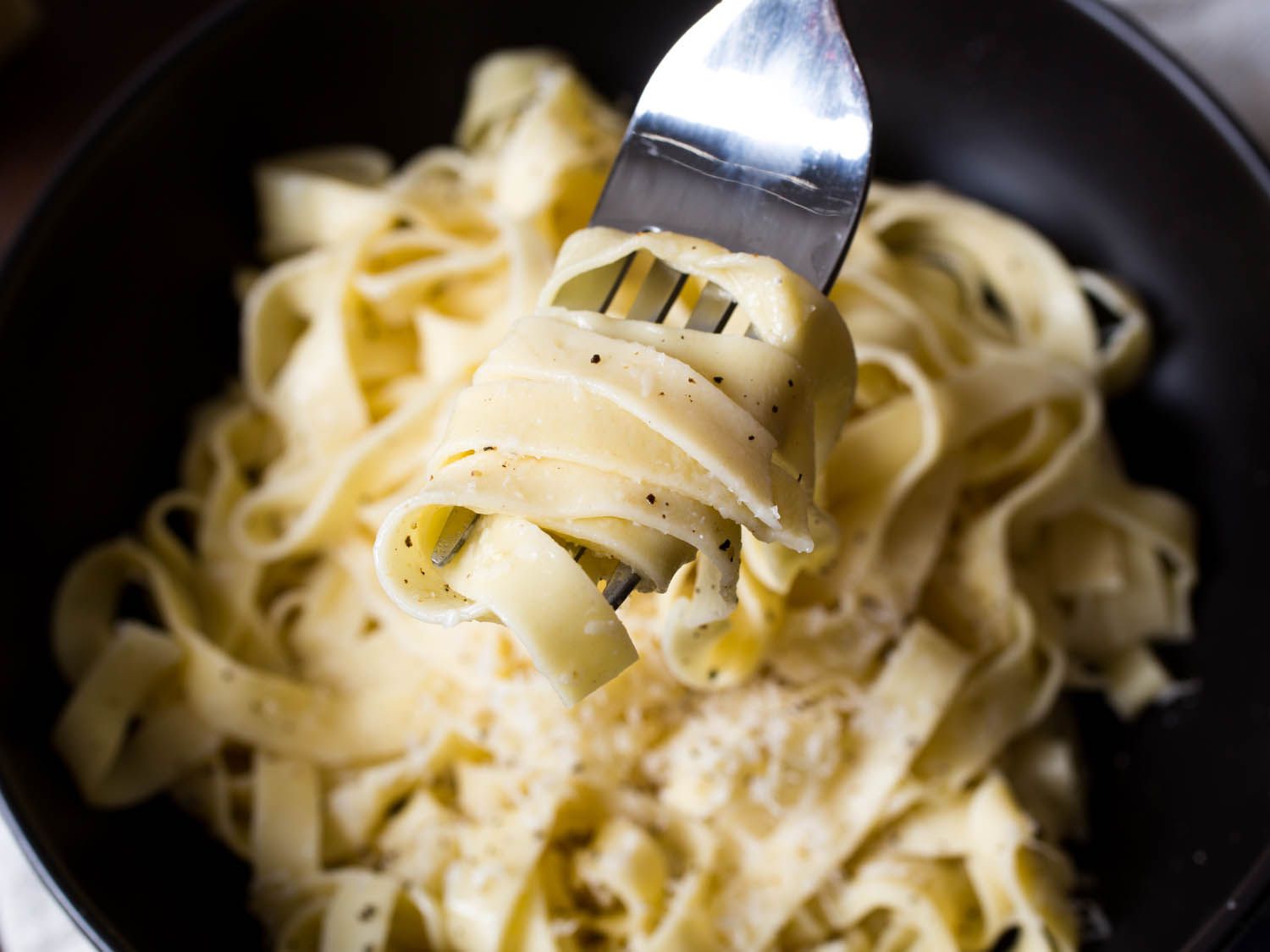 A close up of strands of fresh pasta held up by a fork. 