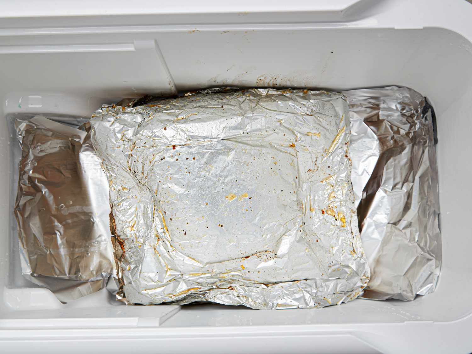 Overhead view of meat wrapped in foil in cooler