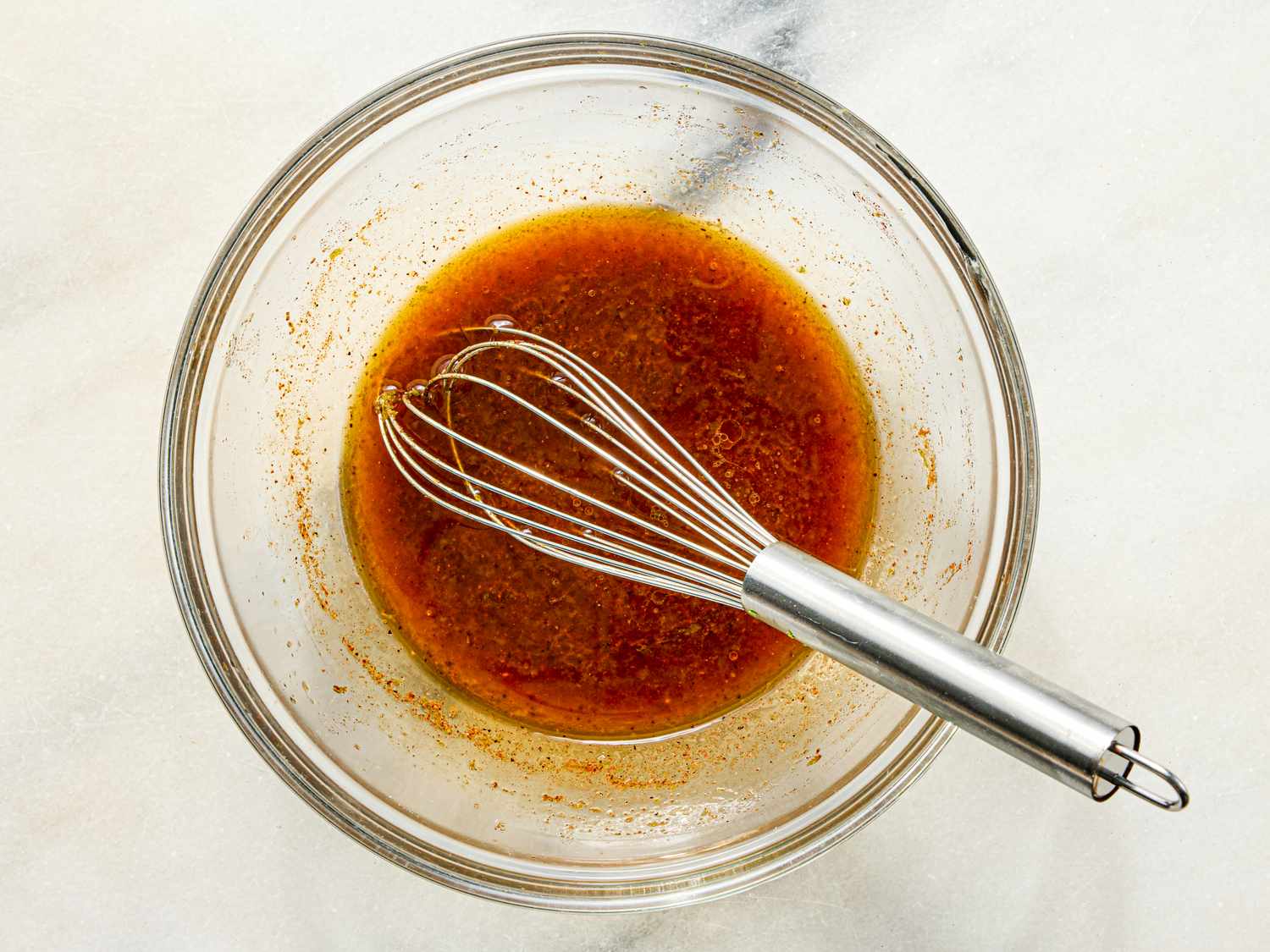 A bowl of dressing with a whisk resting in it