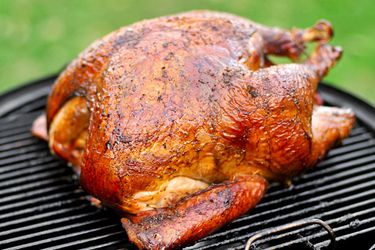 A golden Cajun-style turkey resting on the surface of a charcoal grill.